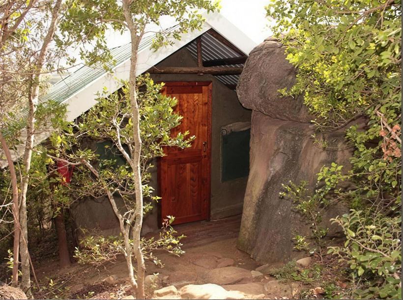 A safari tent at Bush Camp with a hardwood door set against a large sandstone boulder.