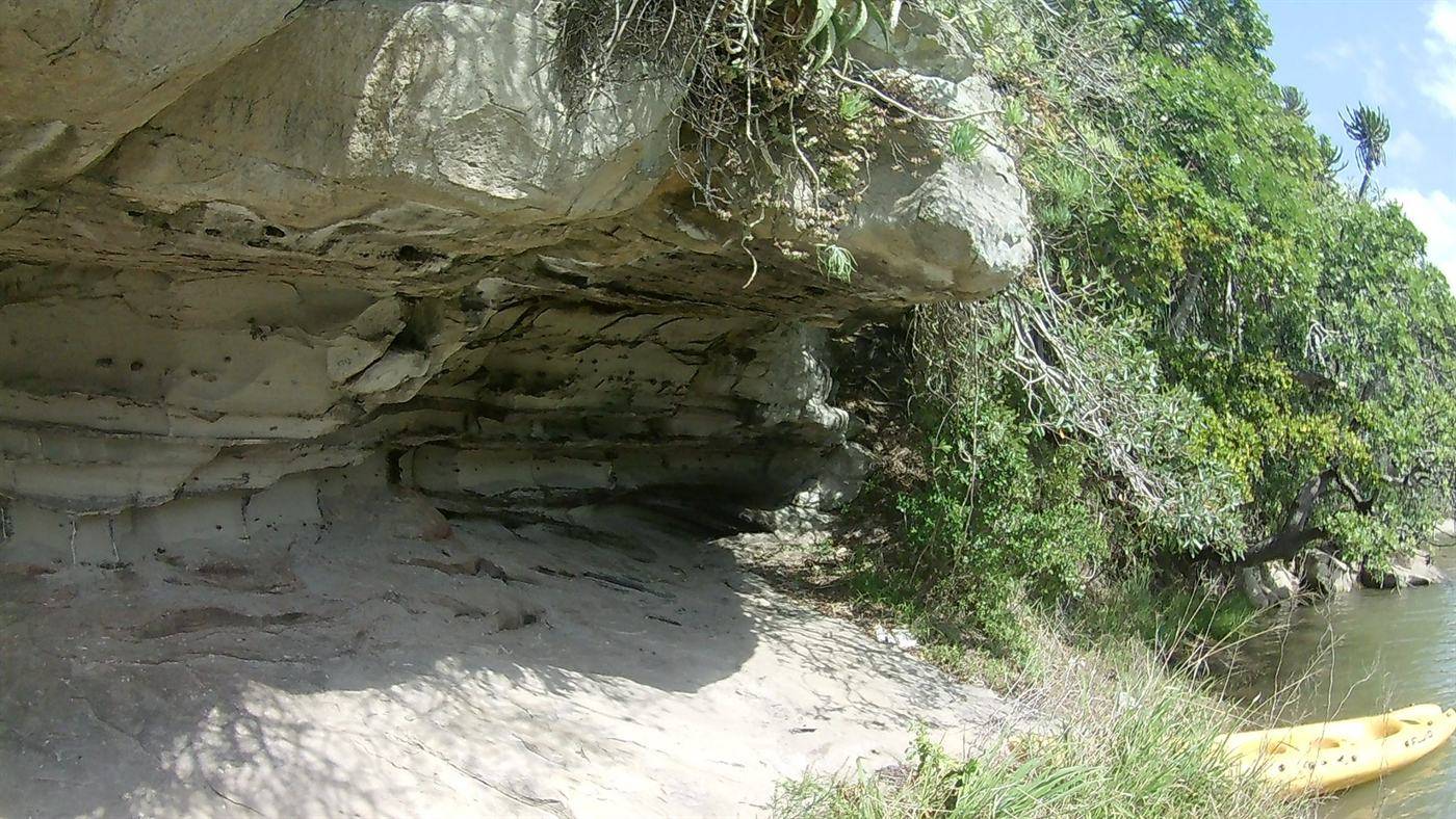 A sandstone overhang above the estuary with a canoe drawn up on the sand below.